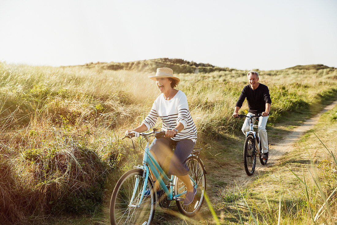 Playful mature couple riding bicycles grass path