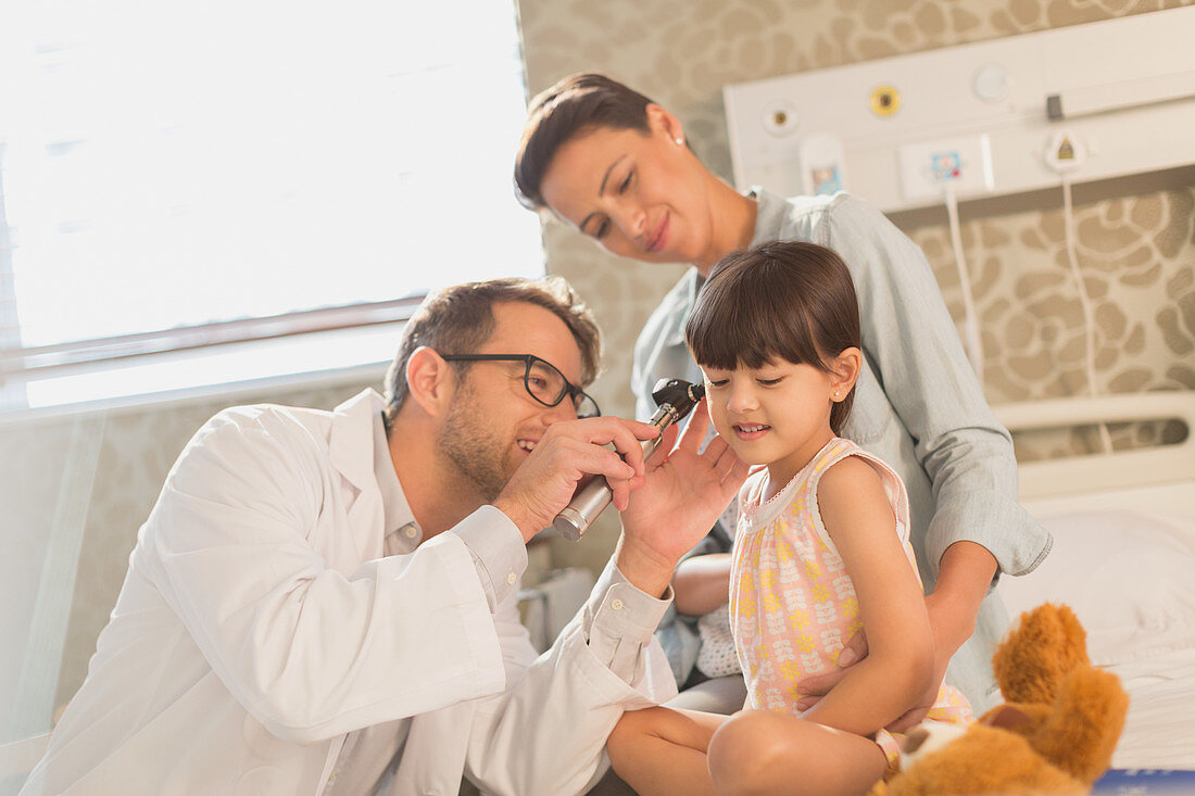 Male doctor using otoscope in ear of girl patient