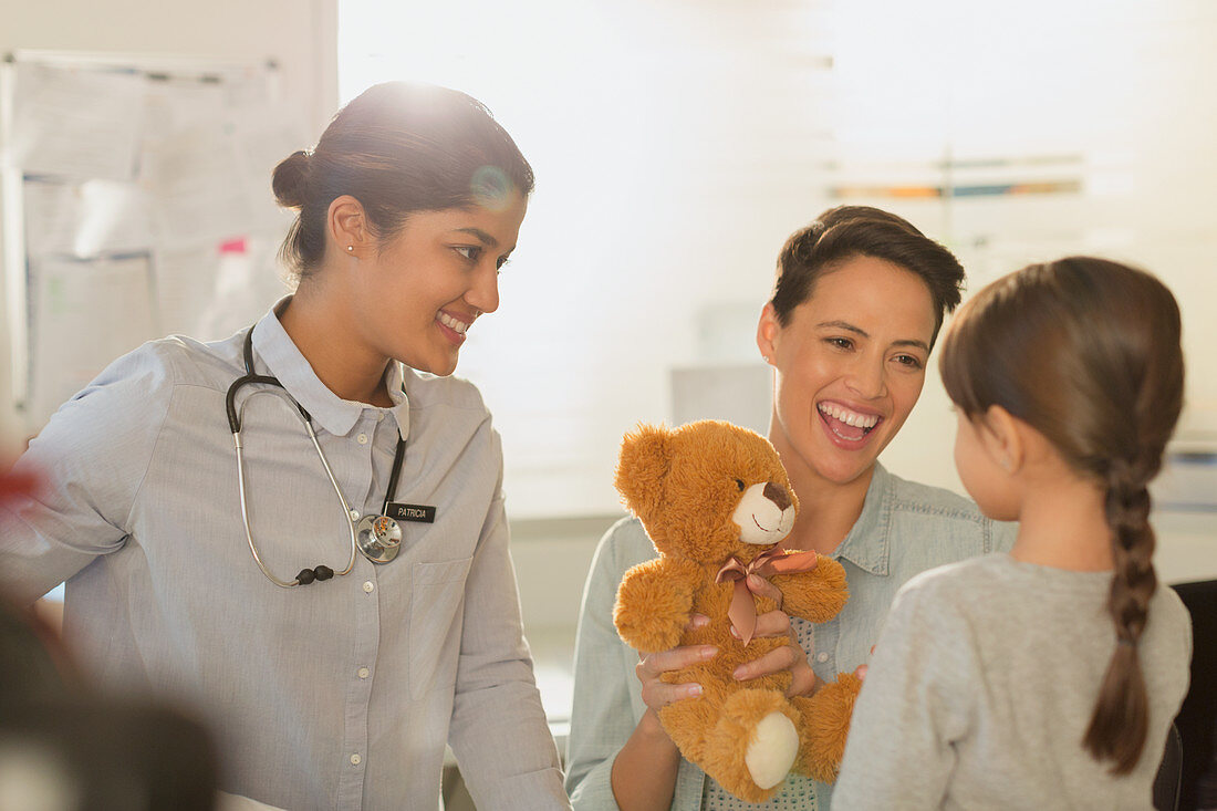 Doctor and mother showing teddy bear to girl