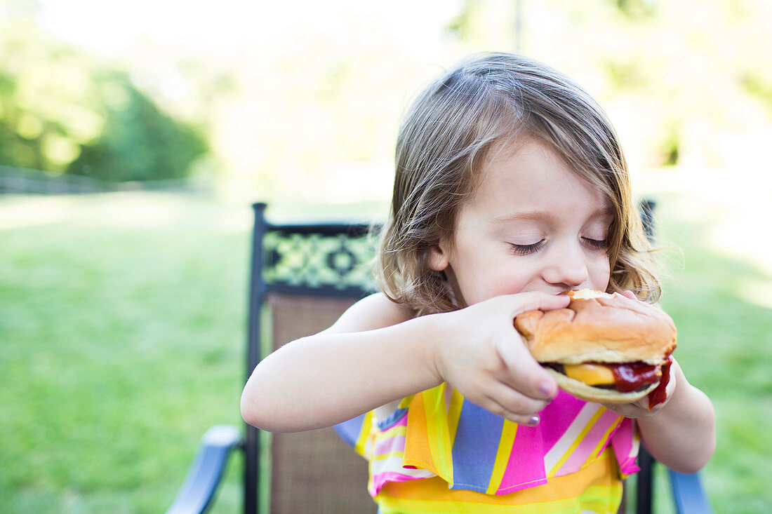 Preschool girl eating messy cheeseburger on patio
