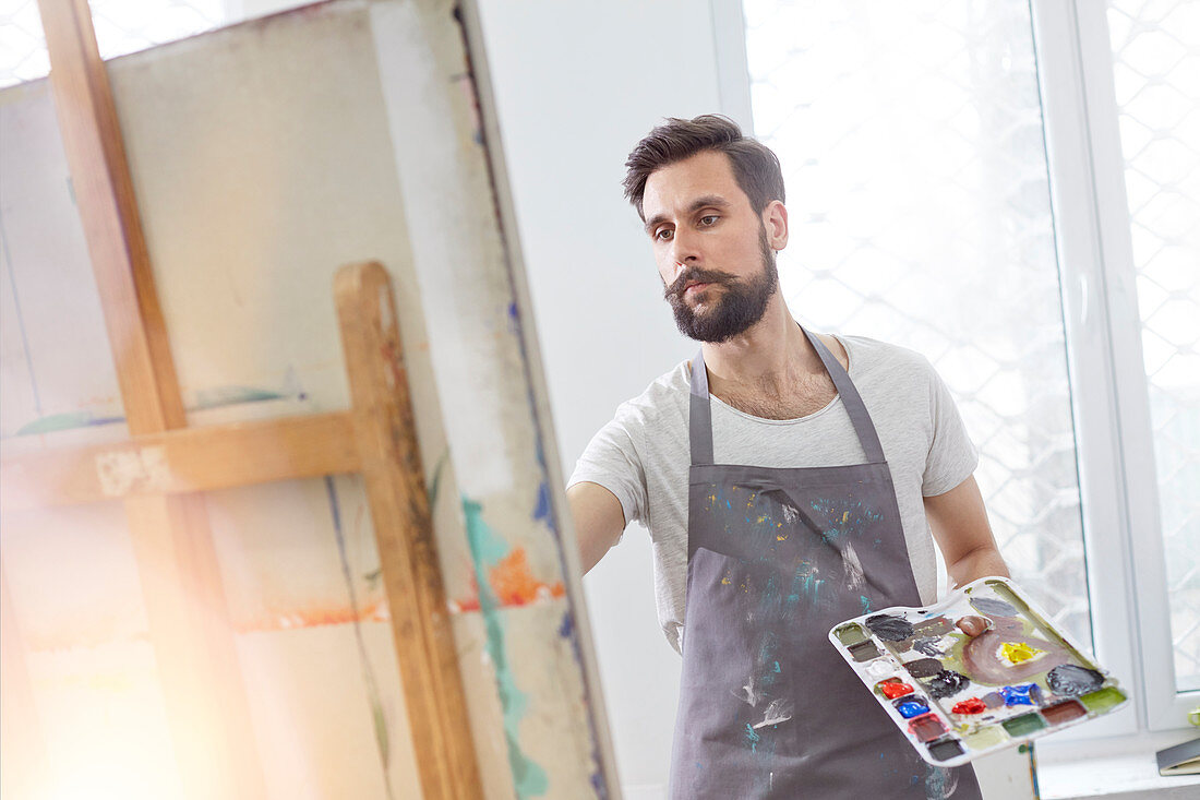 Male artist with palette painting at easel