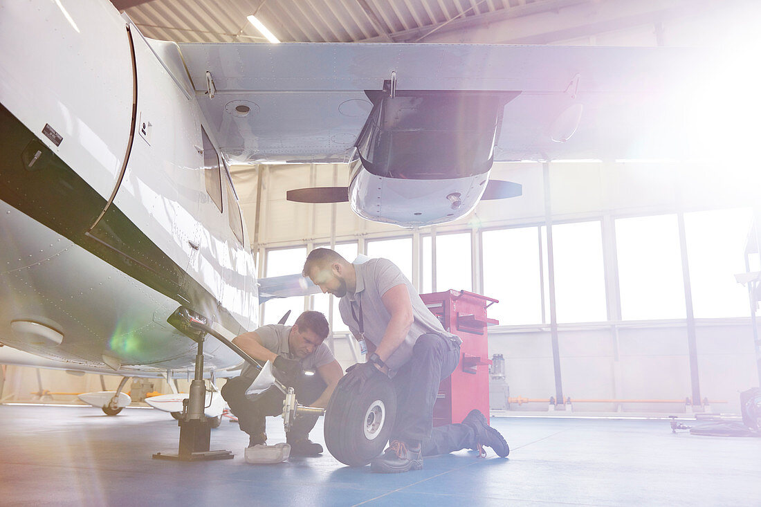 Male mechanics fixing wheels on airplane in hangar