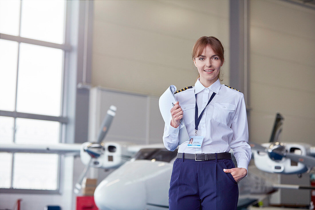 Portrait pilot with paperwork in airplane hangar