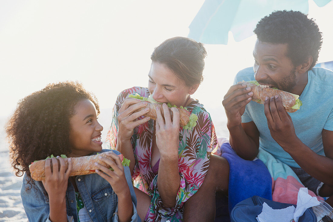 Playful family eating baguette sandwiches on beach