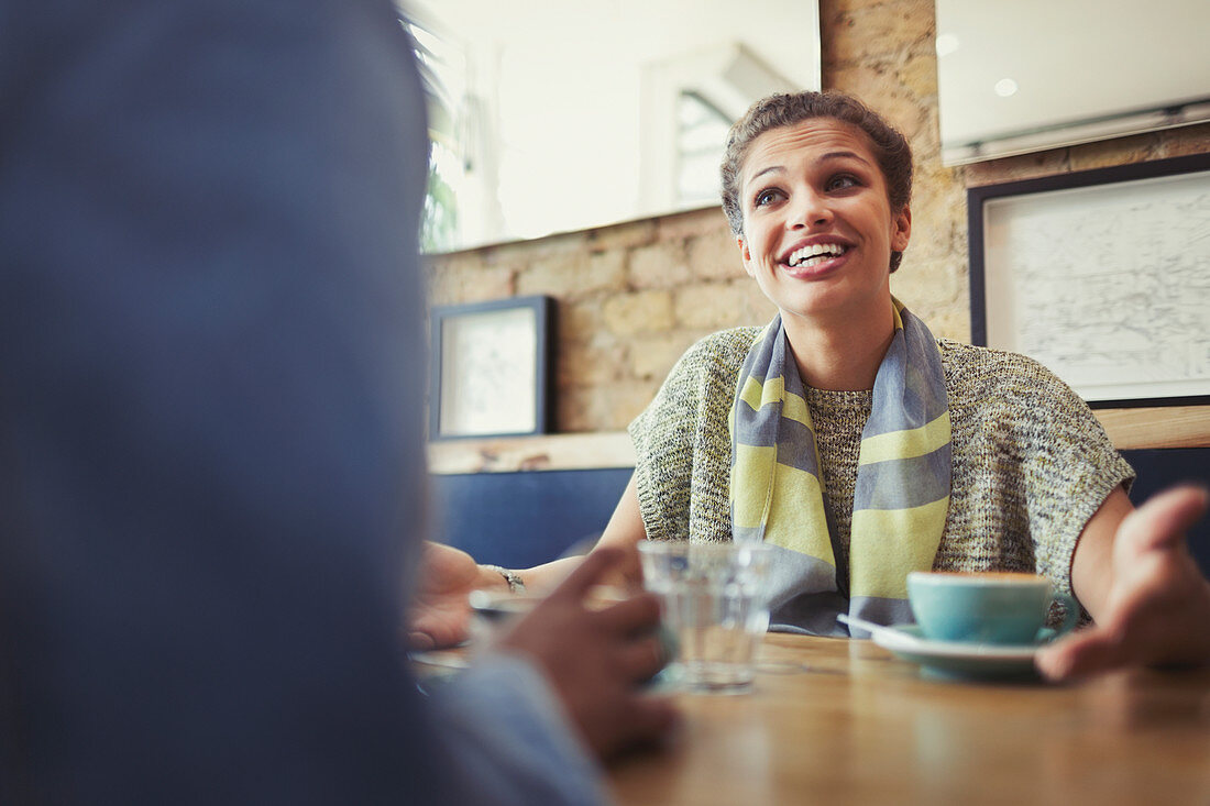 Smiling woman talking to friend, drinking coffee