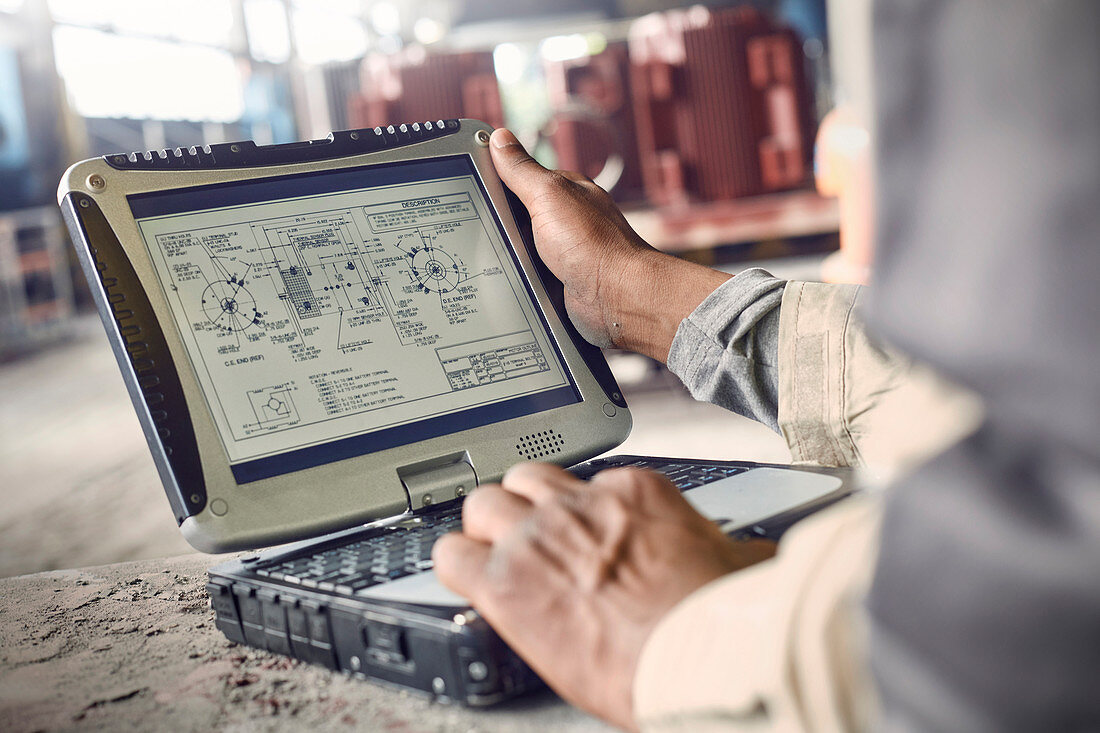 Engineer using laptop, reviewing blueprints
