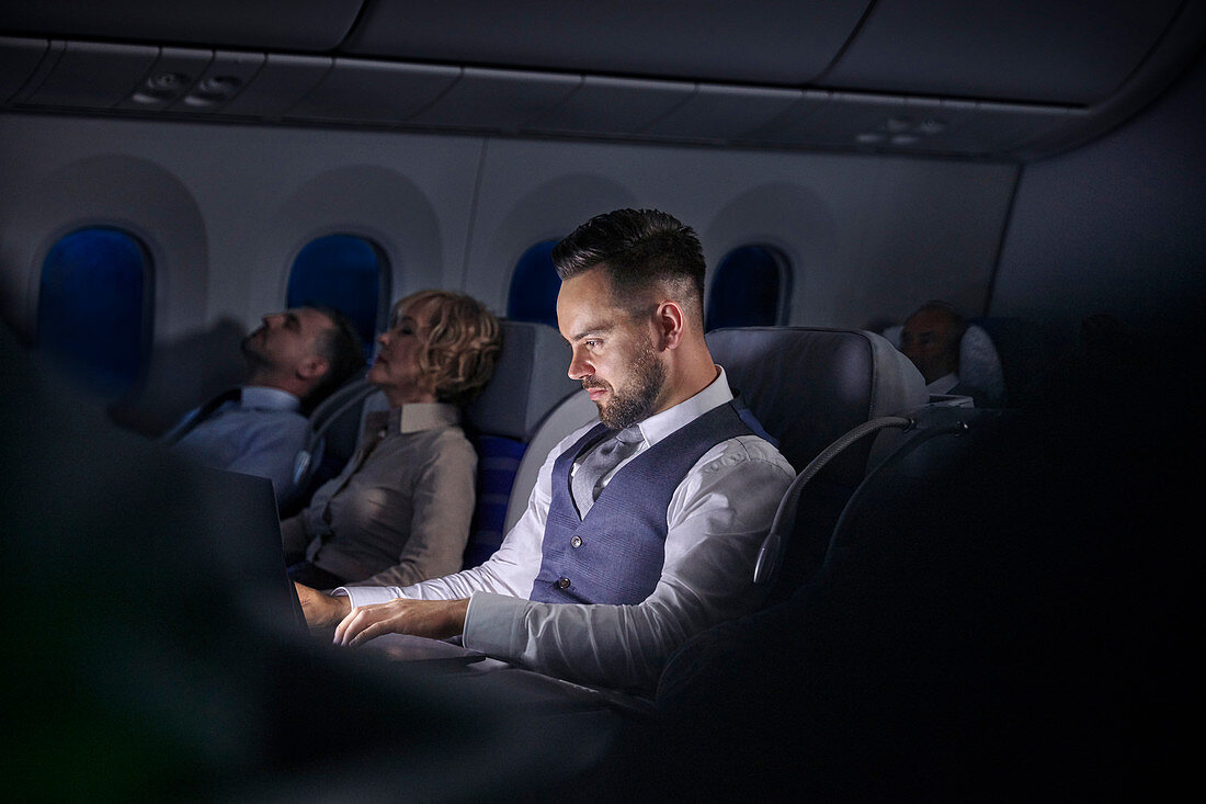 Businessman working on laptop on night airplane