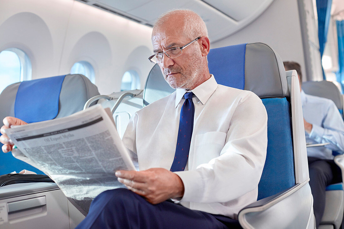 Senior businessman reading newspaper on airplane