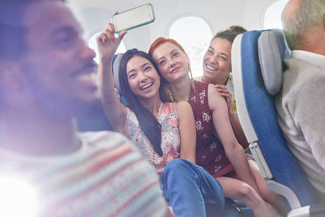 Young women friends taking selfie on airplane