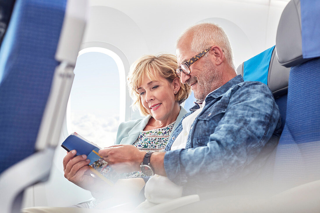 Mature couple reading guidebook on airplane
