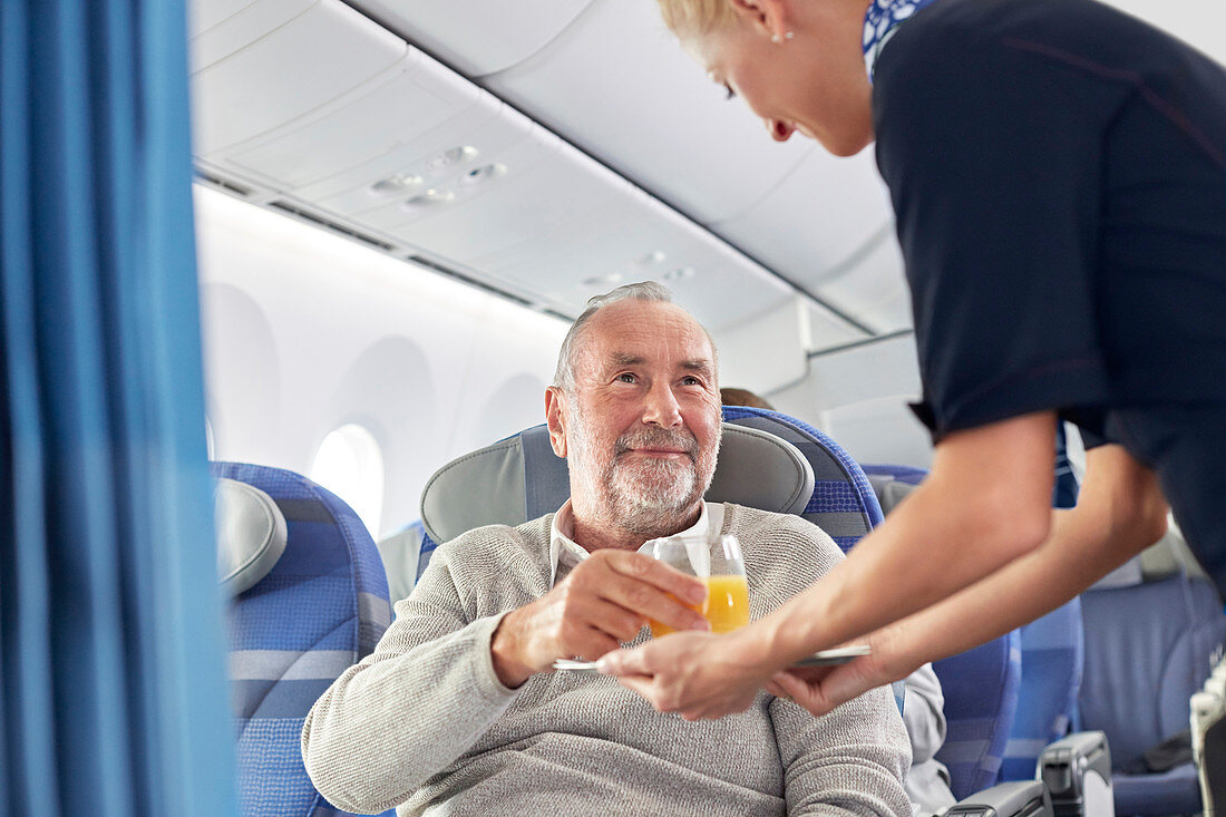 Flight attendant serving orange juice to man