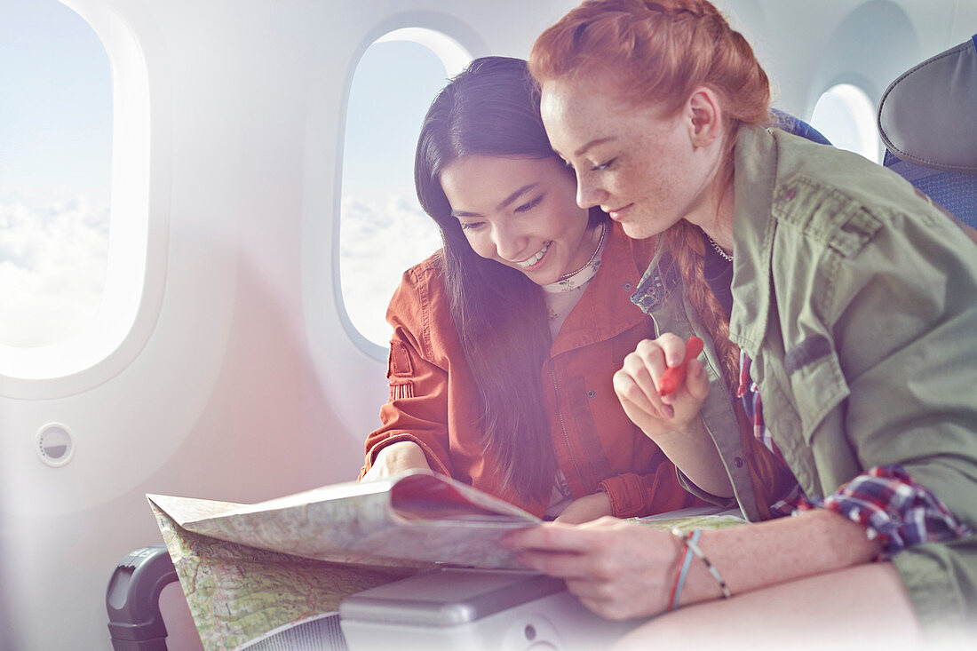 Young women friends looking at map on airplane
