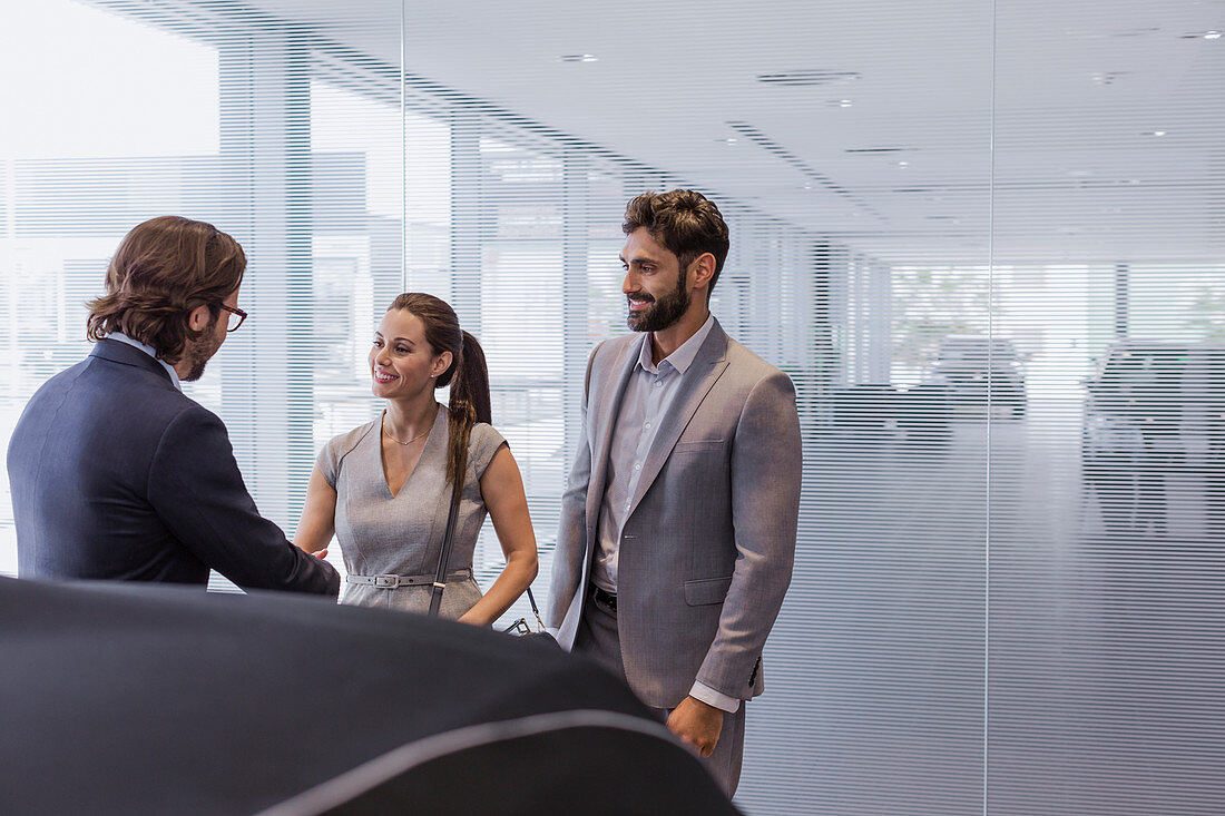 Car salesman greeting couple customers in showroom