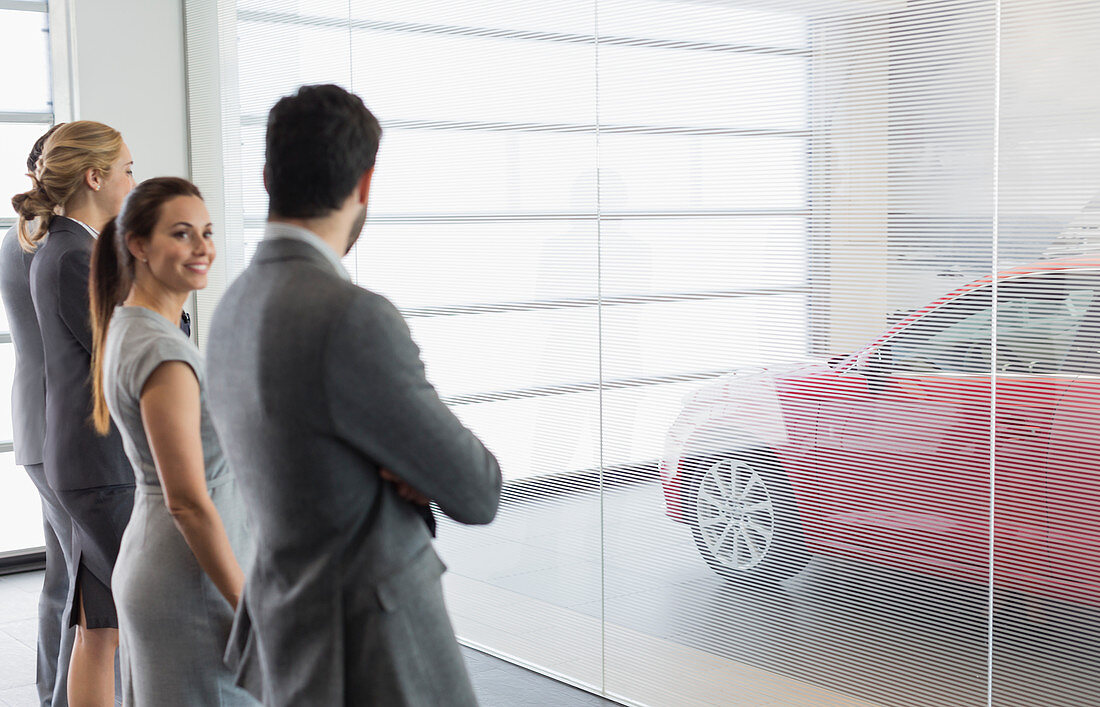 Car sales people looking at new, red car