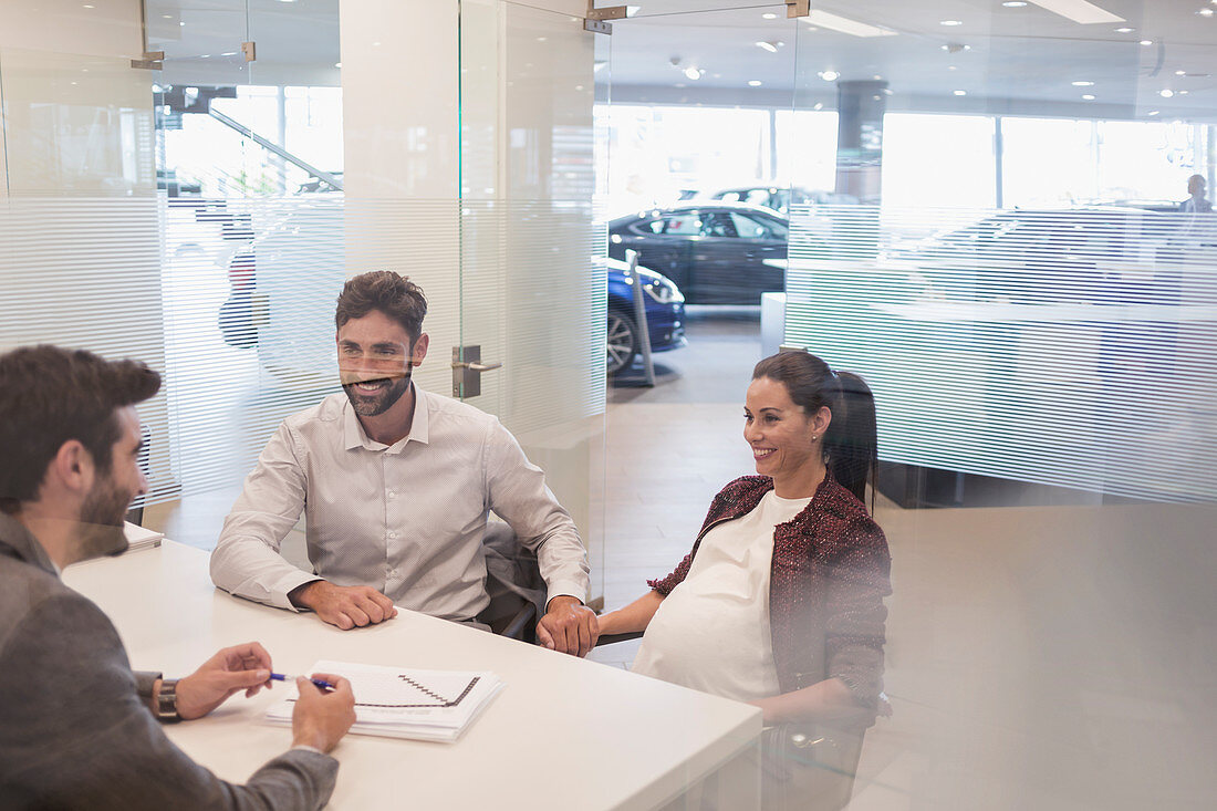 Car salesman talking to pregnant couple in office