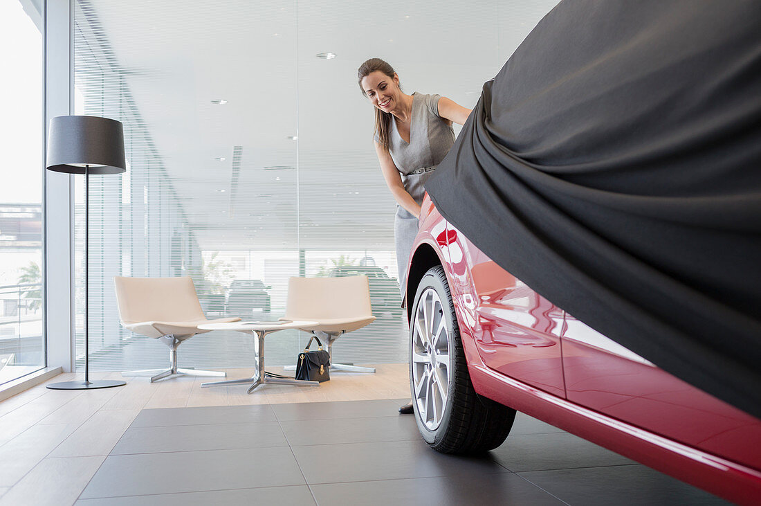 Car saleswoman removing cover from car in showroom