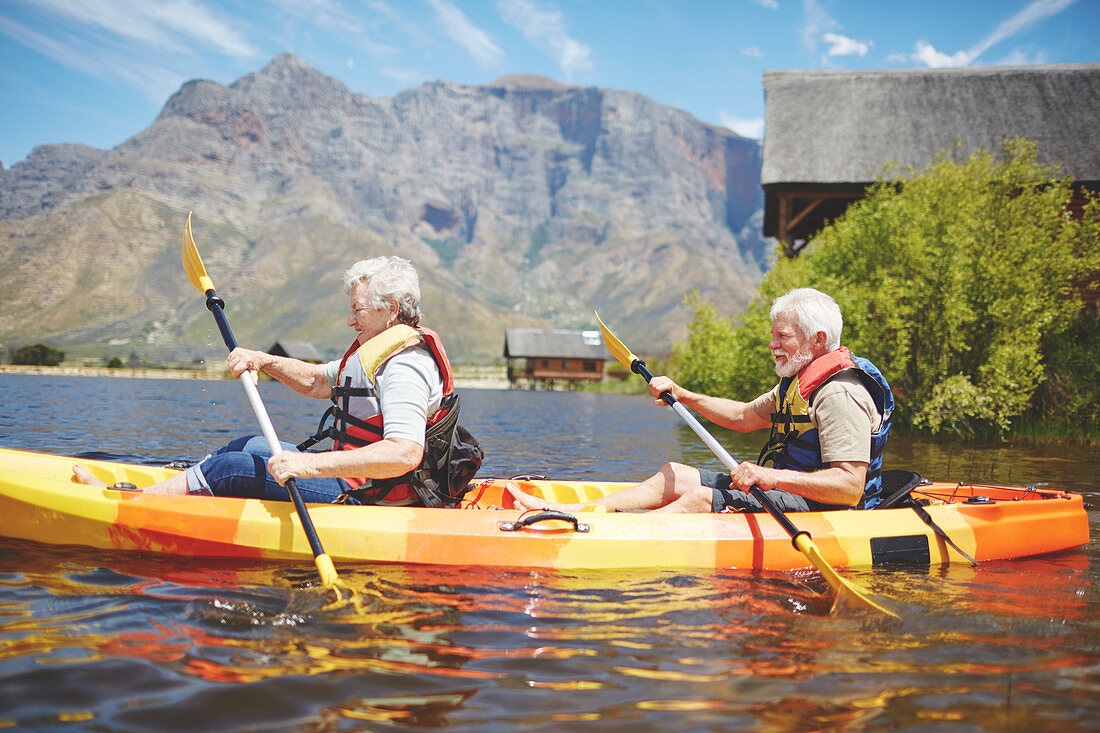 Active senior couple kayaking on sunny summer lake