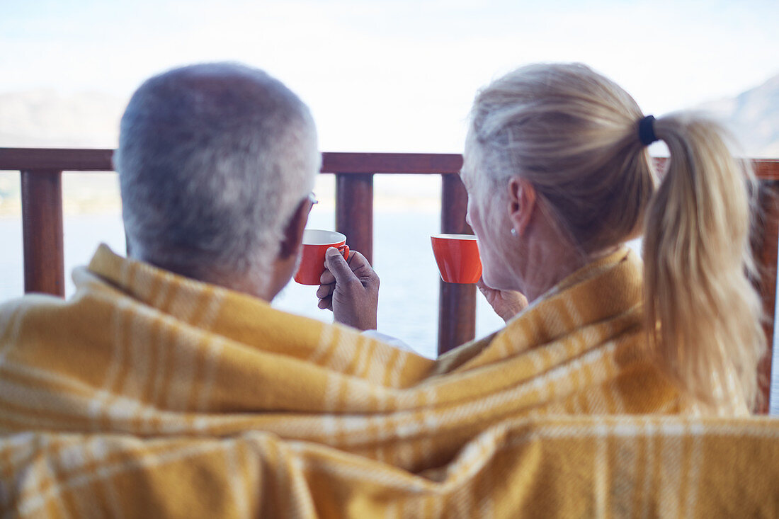 Cosy couple wrapped in blanket, drinking coffee