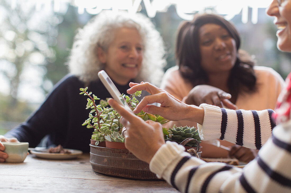 Smiling women friends with smart phone in cafe