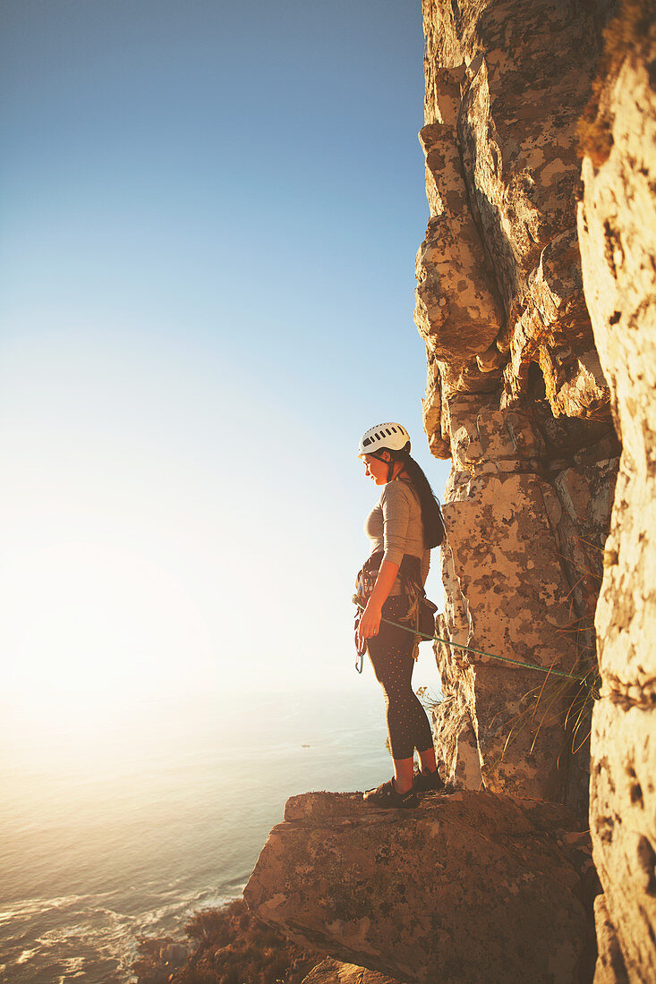 Female rock climber looking at sunny ocean view