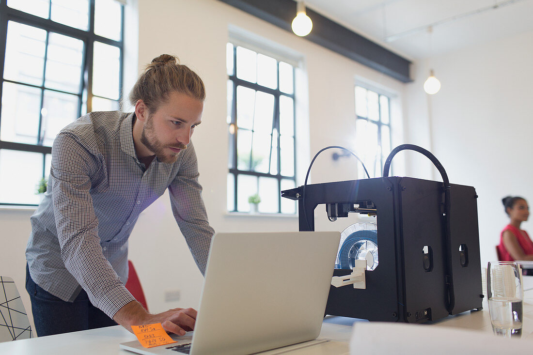 Male designer working at laptop next to 3D printer