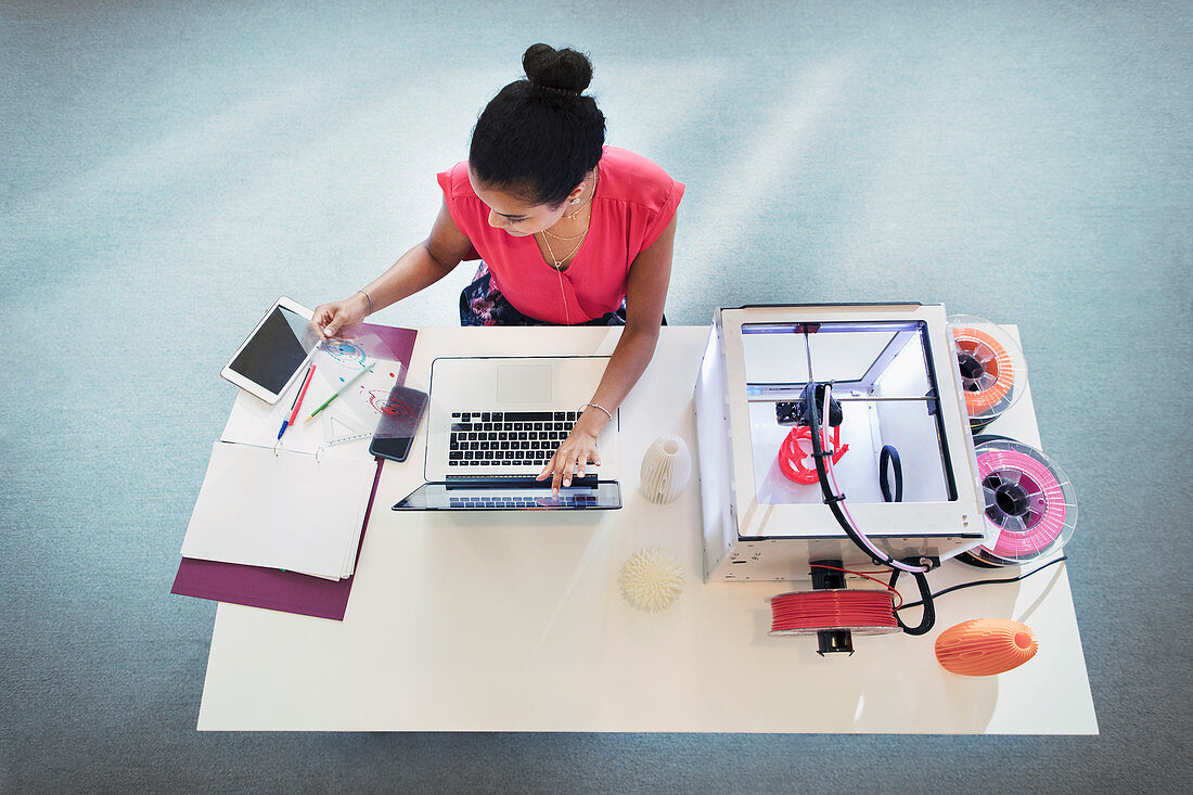 Female designer at laptop next to 3D printer