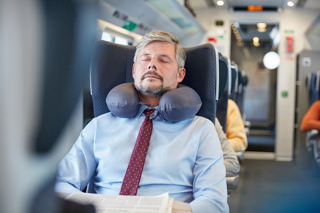 Tired businessman with neck pillow on train