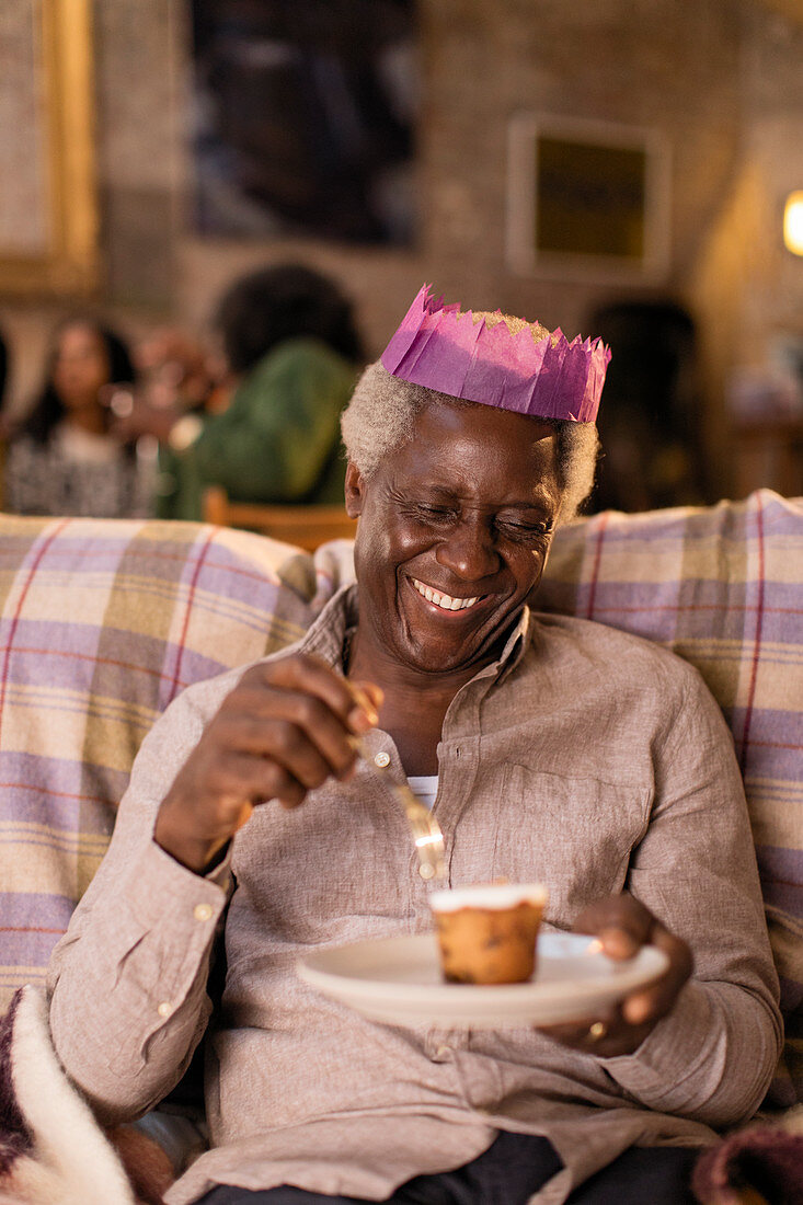 Senior man in Christmas paper crown eating dessert
