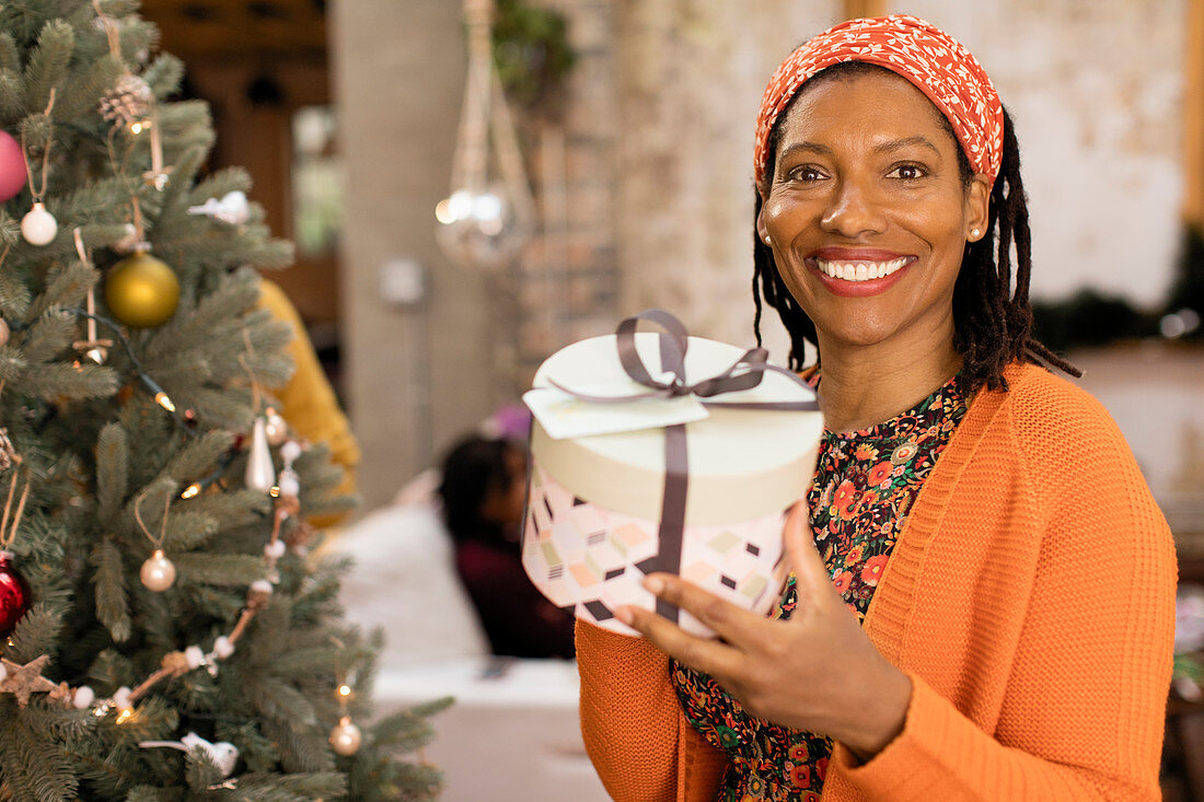 Portrait woman holding gift next to Christmas tree
