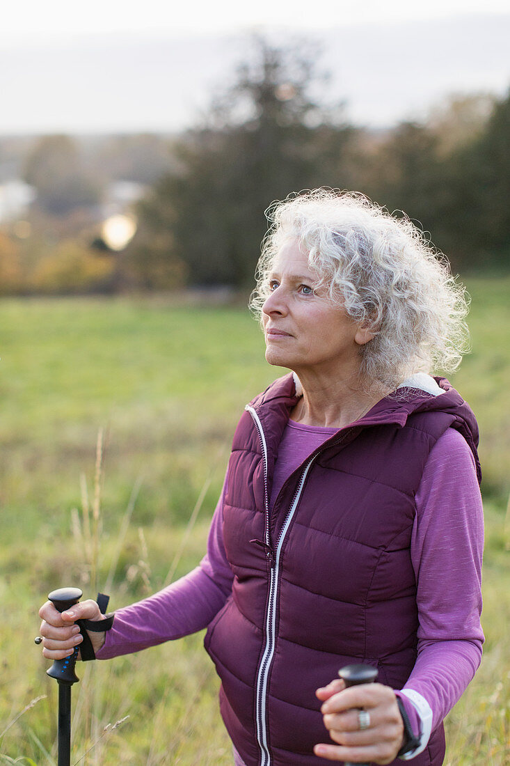 Thoughtful active senior woman hiking with poles