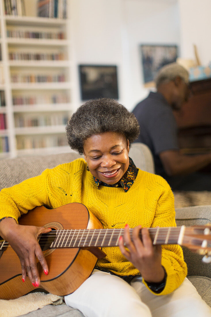 Smiling senior woman playing guitar on sofa