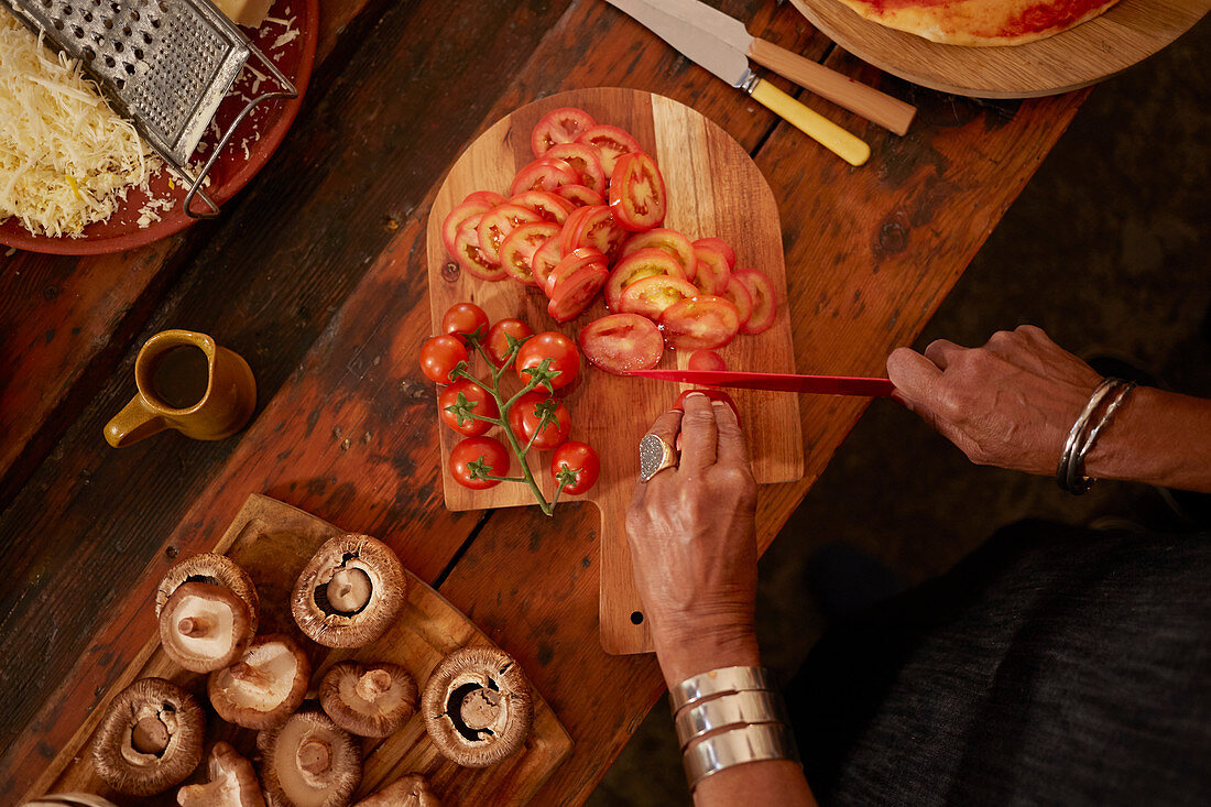 Overhead view woman slicing fresh tomatoes for pizza