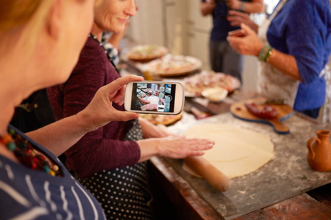 Woman photographing friend making pizza dough