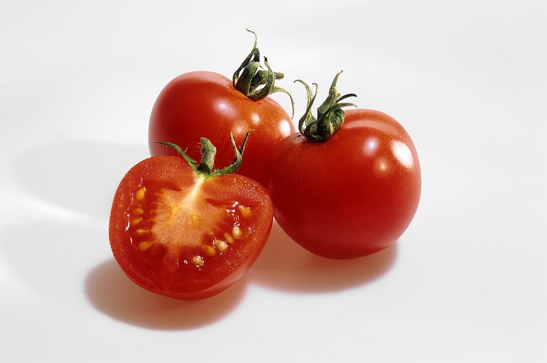 Two whole and one half tomato against white background