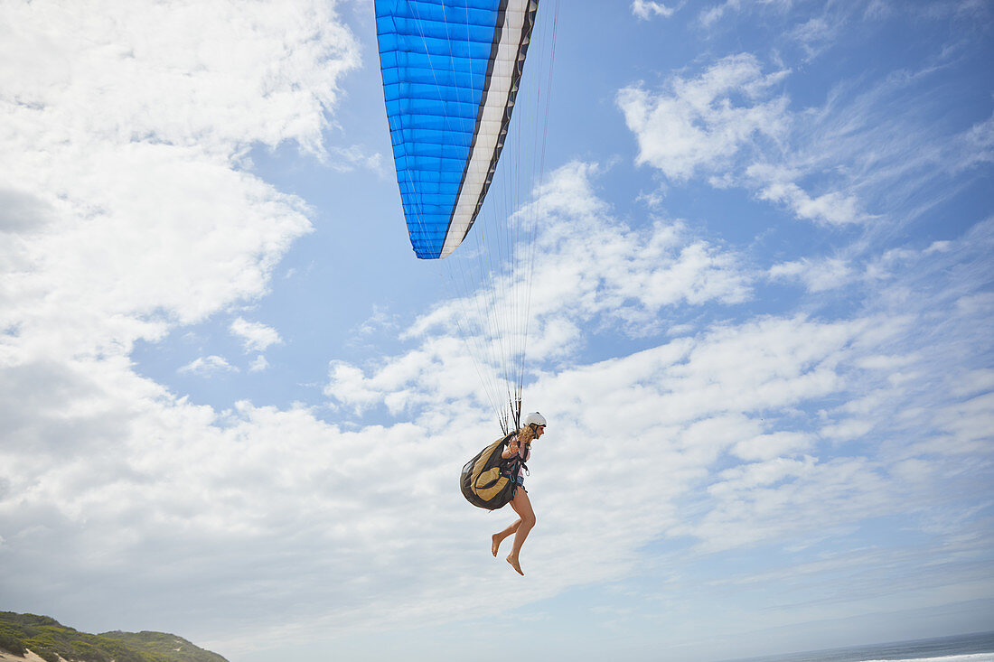 Female paraglider paragliding against blue sky