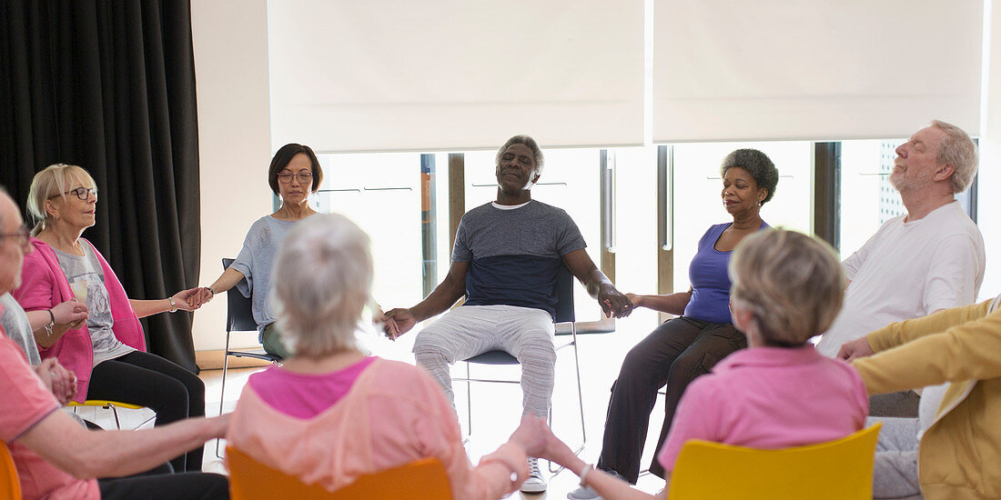 Serene active seniors holding hands, meditating