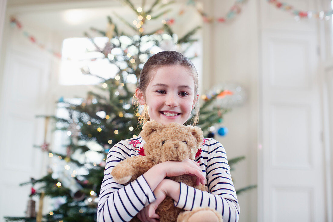 Girl holding teddy bear in front of Christmas tree
