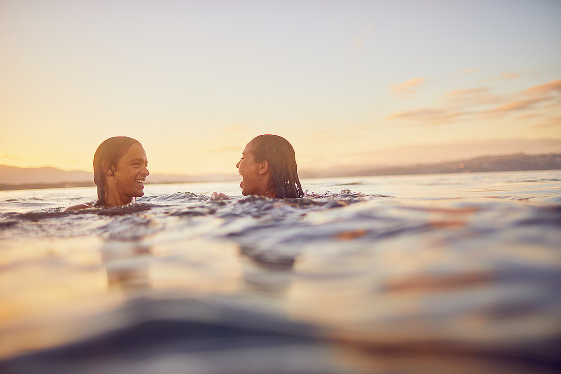 Young couple swimming in ocean at sunset