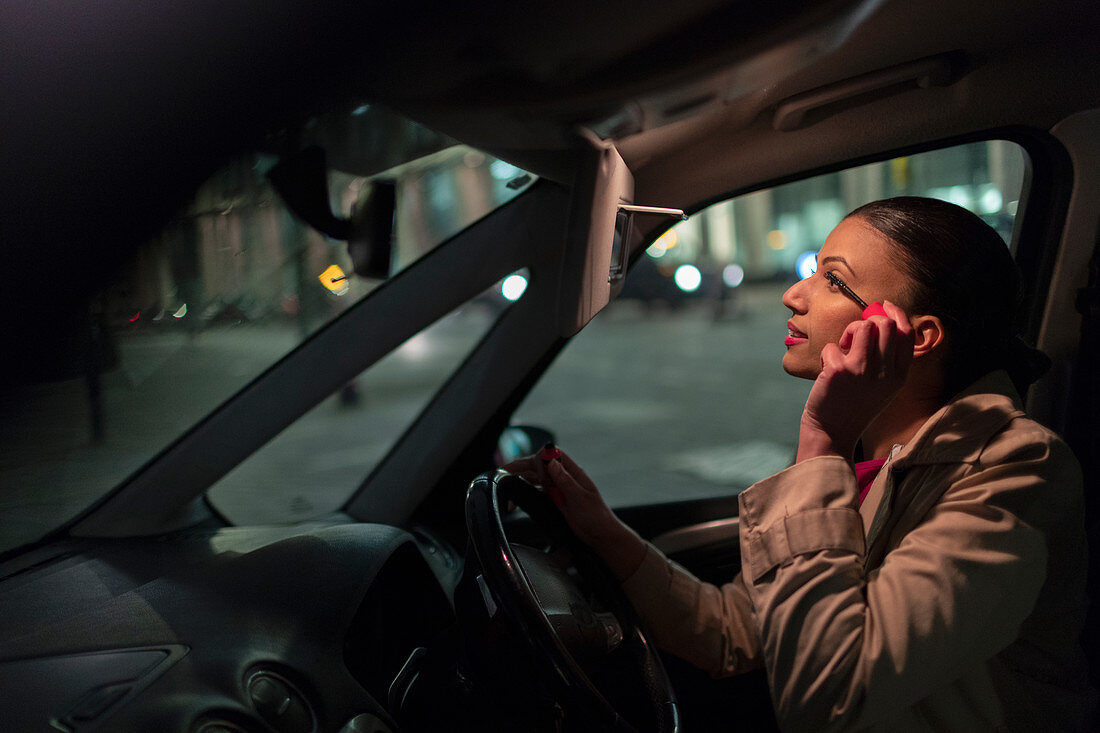Businesswoman applying mascara in car at night