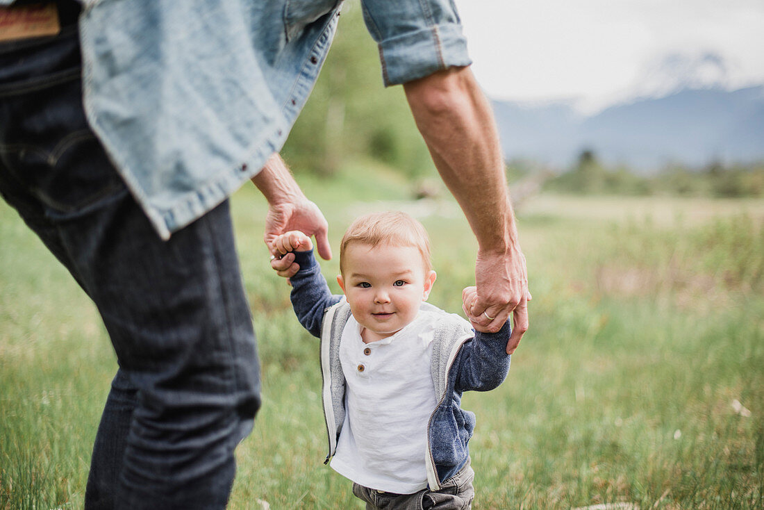 Father walking with baby son in grassy field