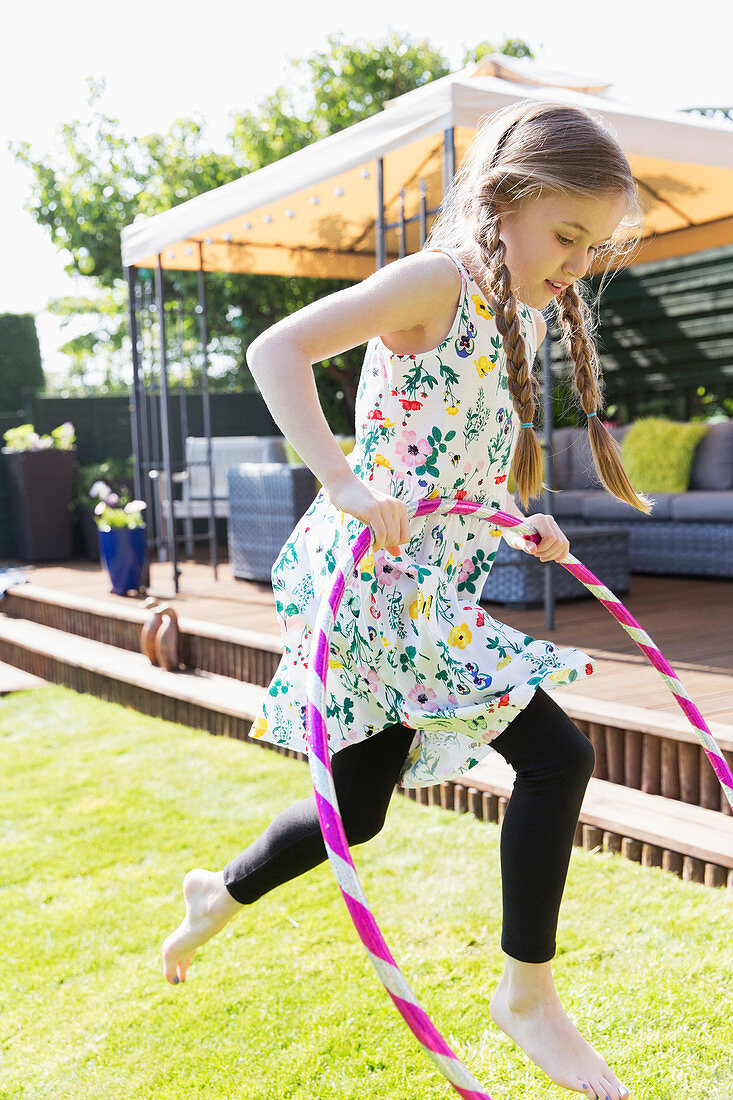 Girl playing with plastic hoop in sunny backyard