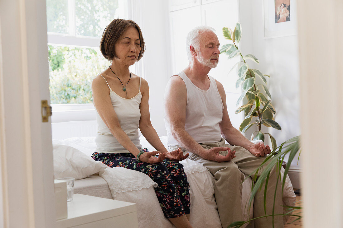 Serene senior couple meditating on bed