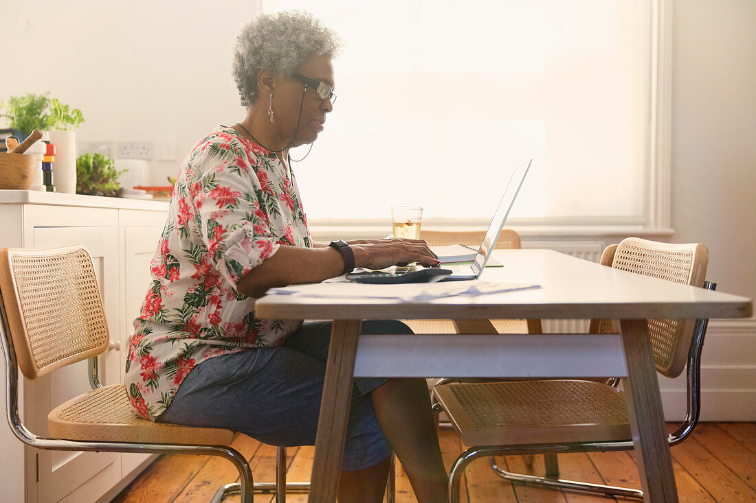 Senior woman paying bills at laptop in kitchen