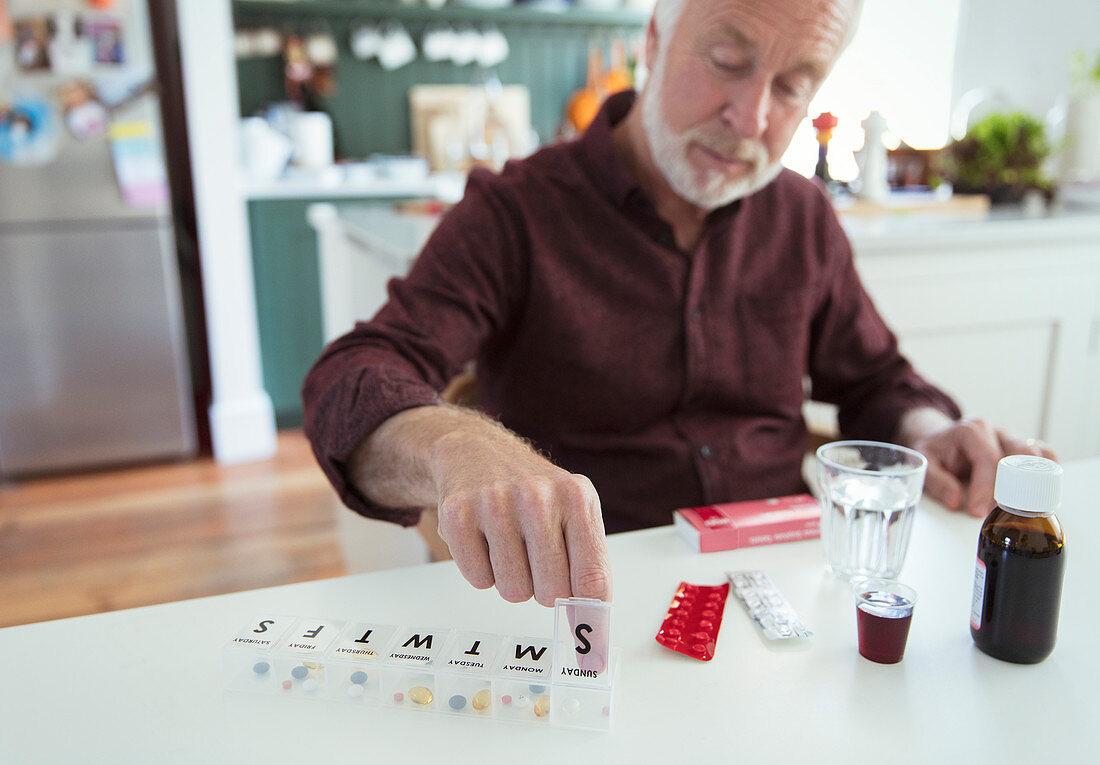 Senior man organizing pill box at kitchen table