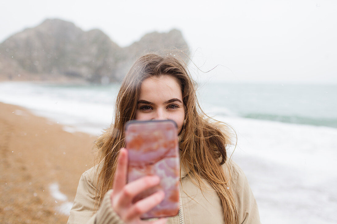 Teenage girl taking selfie on winter ocean beach