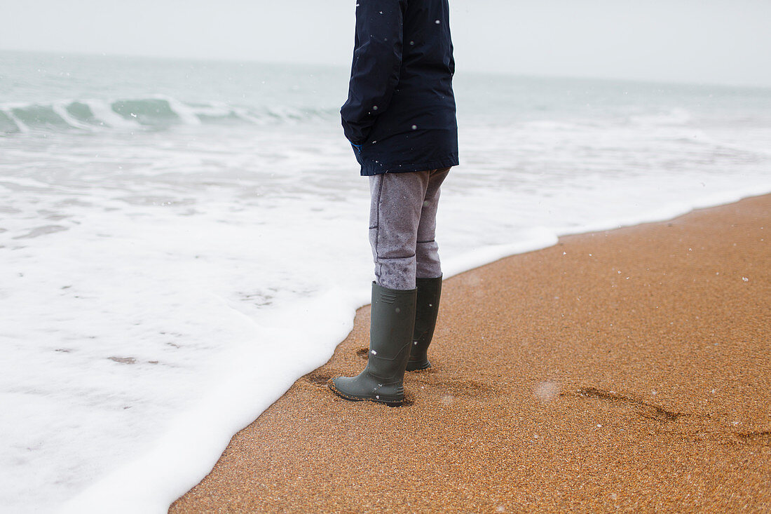 Boy in rubber boots standing on winter beach