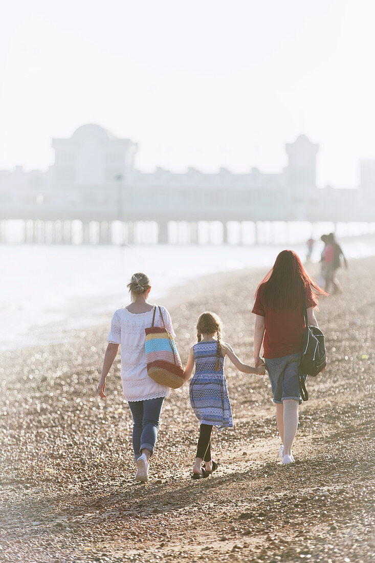 Lesbian couple and daughter holding hands on beach