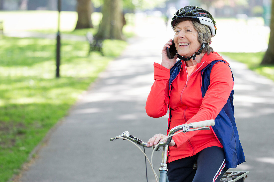 Active senior woman talking on cell phone on bike