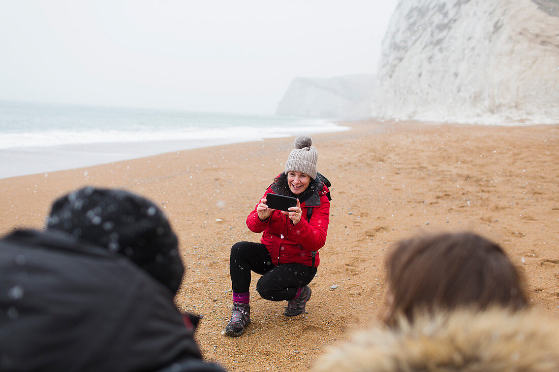 Mother photographing kids on snowy winter beach