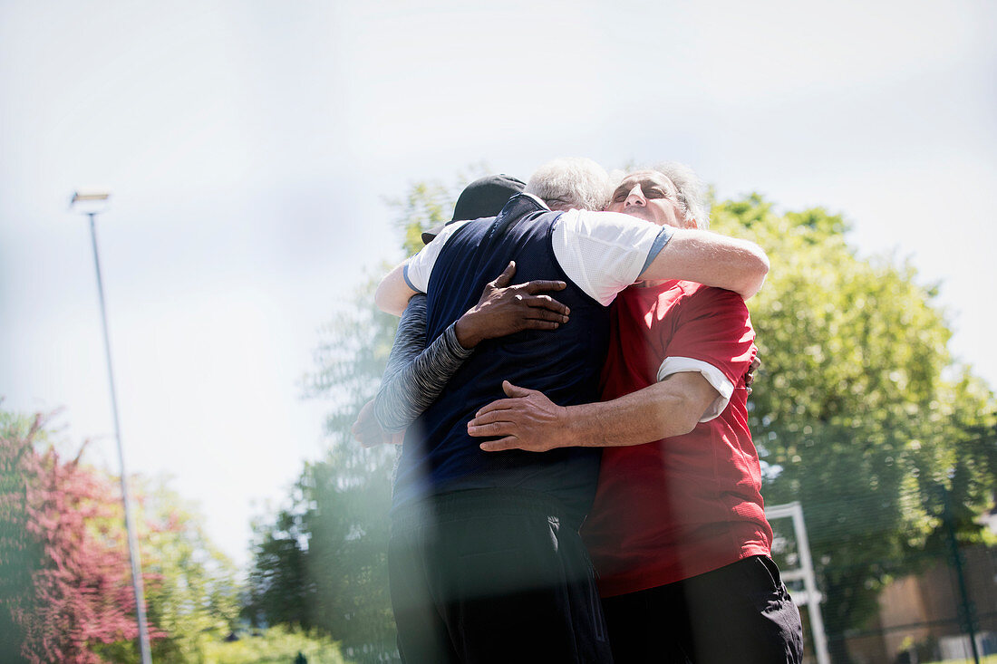 Active senior men friends hugging in park